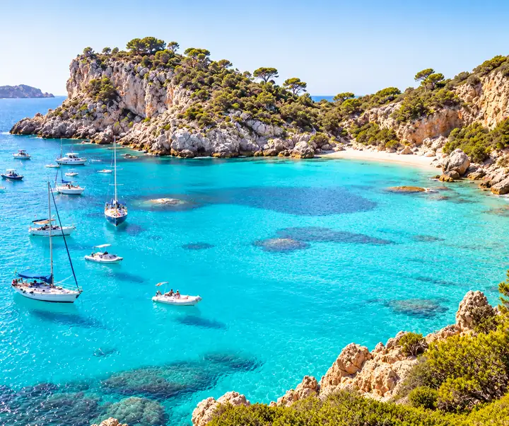 Turquoise travel bay with boats and a sunlit rocky coastline